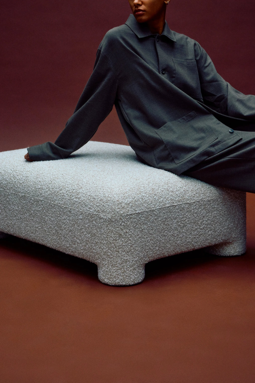 Person sitting on a textured ottoman against a red background
