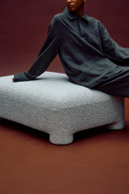 Person sitting on a textured ottoman against a red background