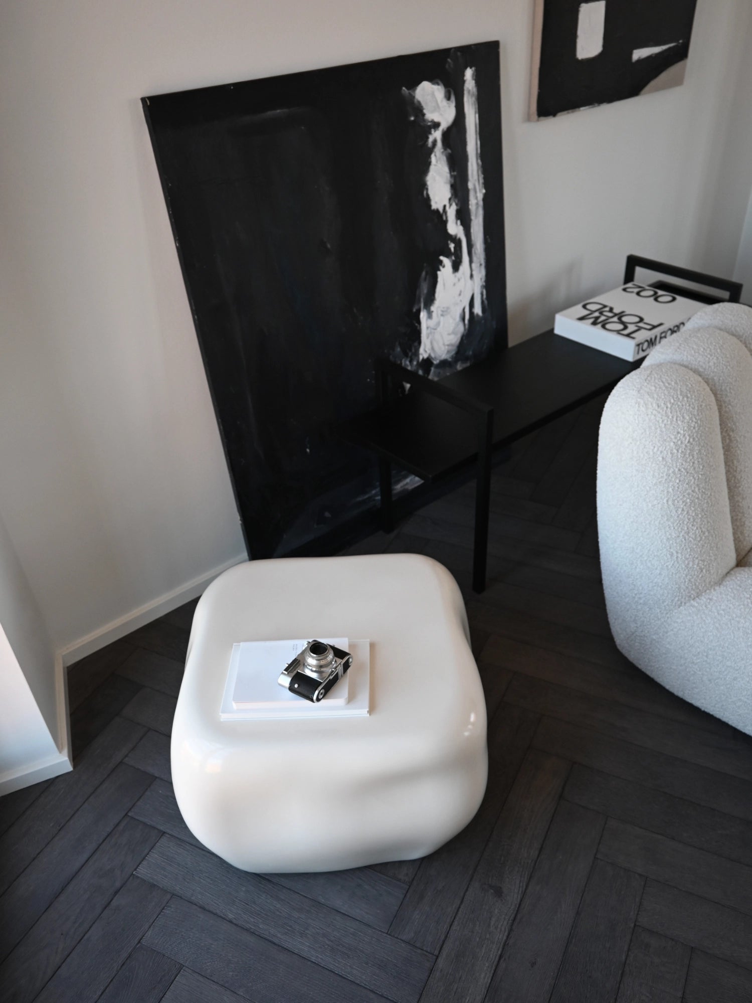 101 CPH Ishi Coffee Table - Ceramic in a lifestyle close-up, showing its smooth, glossy off-white sculptural form on a dark herringbone floor. A premium accent for contemporary interiors.