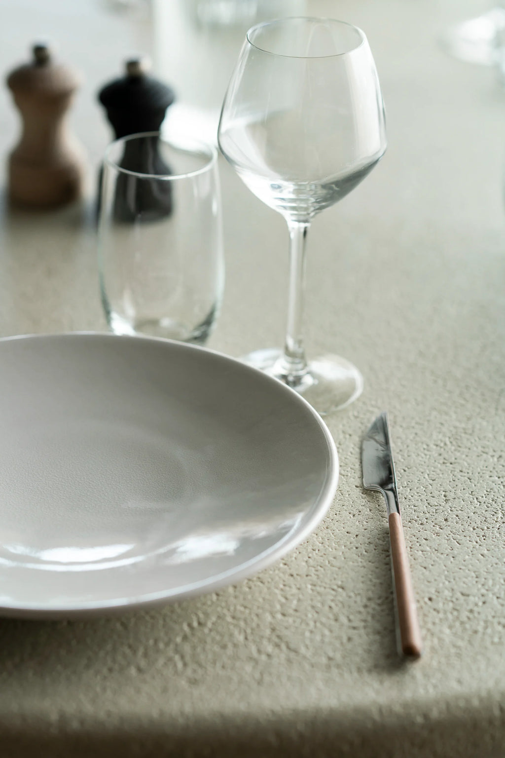 Ethnicraft Elements Dining Table, a modern minimalist dining table featuring a light beige textured stone-like surface with a porous finish, evoking a natural, organic modern aesthetic. This contemporary dining room furniture piece is ideal for creating a sophisticated and inviting atmosphere in any dining area or open-plan kitchen.