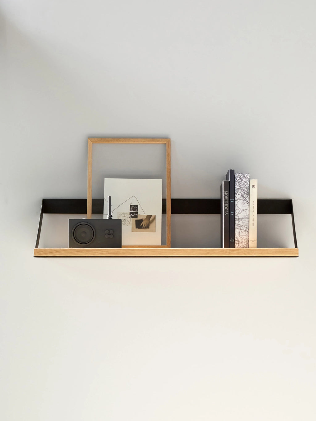 Ethnicraft Ribbon Shelf, a sleek modern minimalist wall shelf featuring a light natural solid oak board supported by a continuous matte black metal bracket that wraps around the back and sides. This contemporary floating shelf offers a clean aesthetic for displaying decor and books. Perfect for Scandinavian living rooms, bedrooms, or modern home office styling.