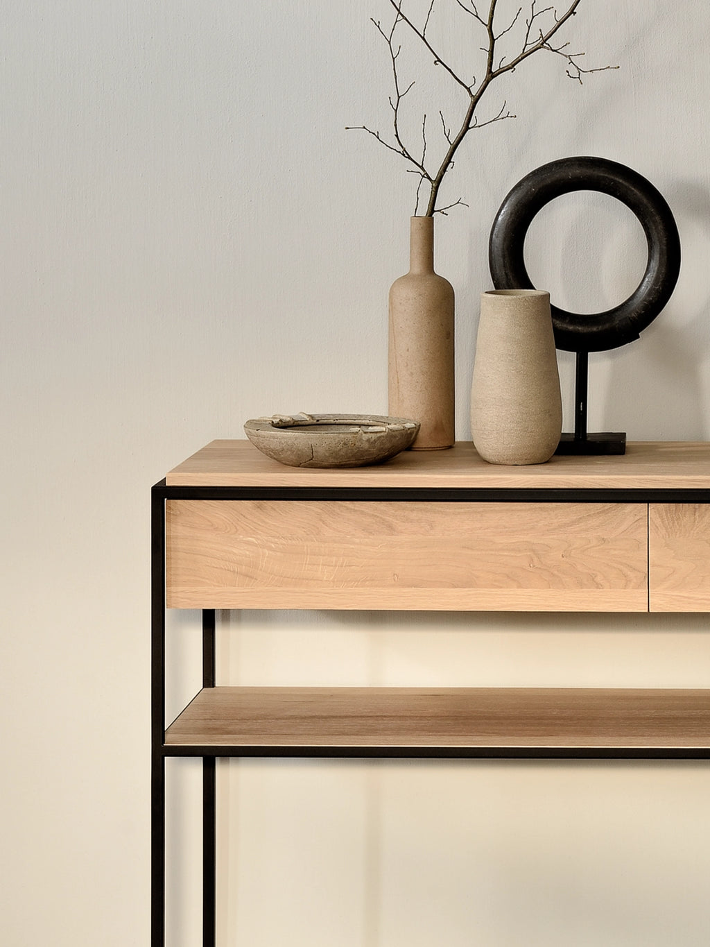 Ethnicraft Monolit Console, a modern minimalist console table featuring a light natural oak wood top and drawer with a sleek matte black metal frame. This contemporary design offers an integrated storage drawer and an open lower shelf for display. Ideal as an industrial chic entryway table or a Scandinavian living room accent.