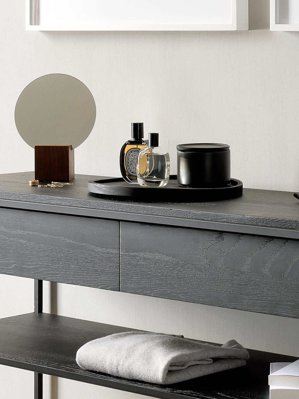 Ethnicraft Monolit Console, a modern minimalist console table featuring a striking black stained oak tabletop and two integrated drawers, showcasing a prominent wood grain texture. Supported by a sleek black metal frame with a lower shelf for additional storage, this contemporary piece offers both style and functionality. Ideal as an entryway console, hallway table, or bedroom dressing table in modern homes.