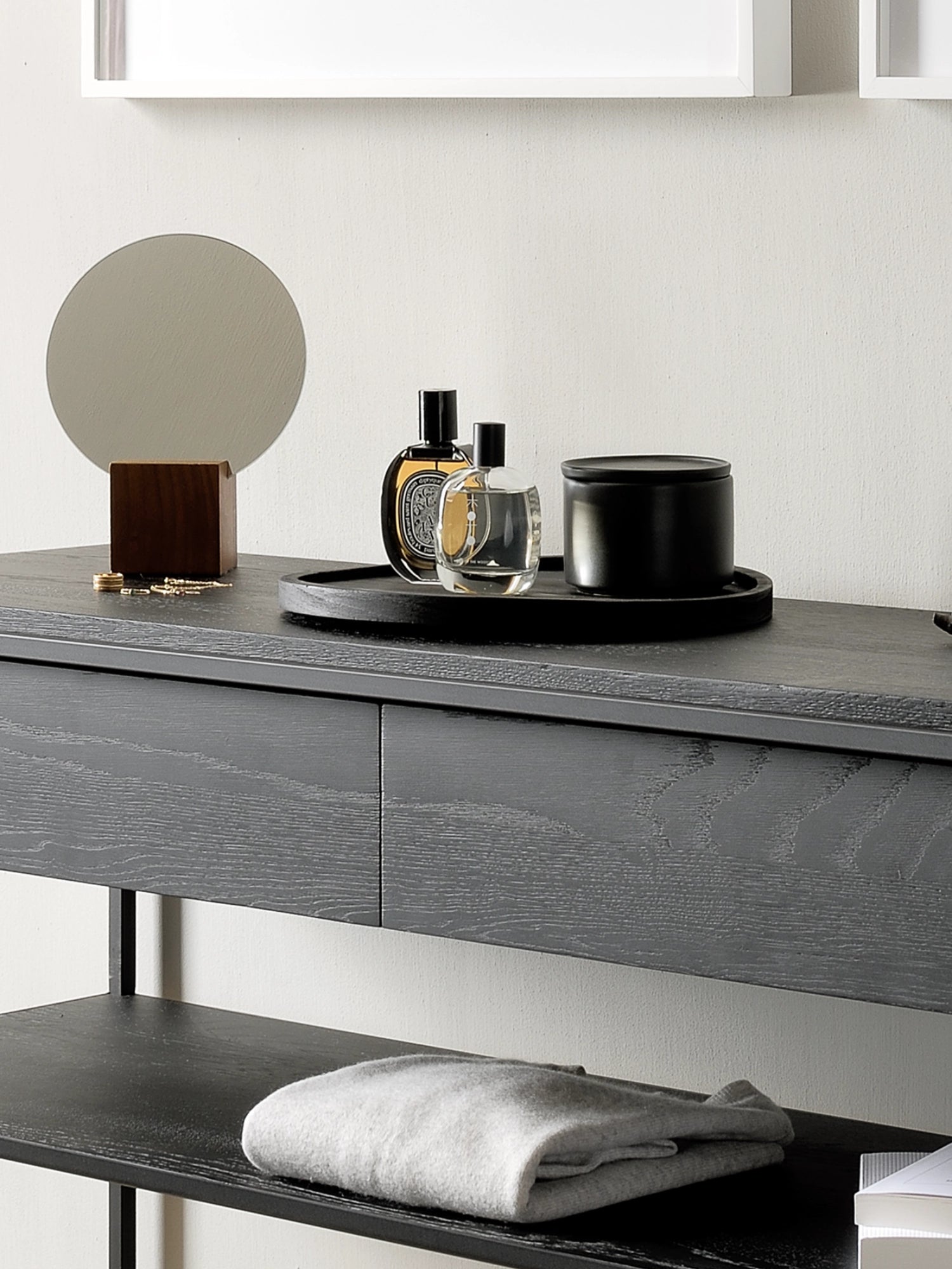 Ethnicraft Monolit Console, a modern minimalist console table featuring a striking black stained oak tabletop and two integrated drawers, showcasing a prominent wood grain texture. Supported by a sleek black metal frame with a lower shelf for additional storage, this contemporary piece offers both style and functionality. Ideal as an entryway console, hallway table, or bedroom dressing table in modern homes.