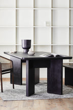 Dark wooden dining table with a vase and open book in a minimalistic room.