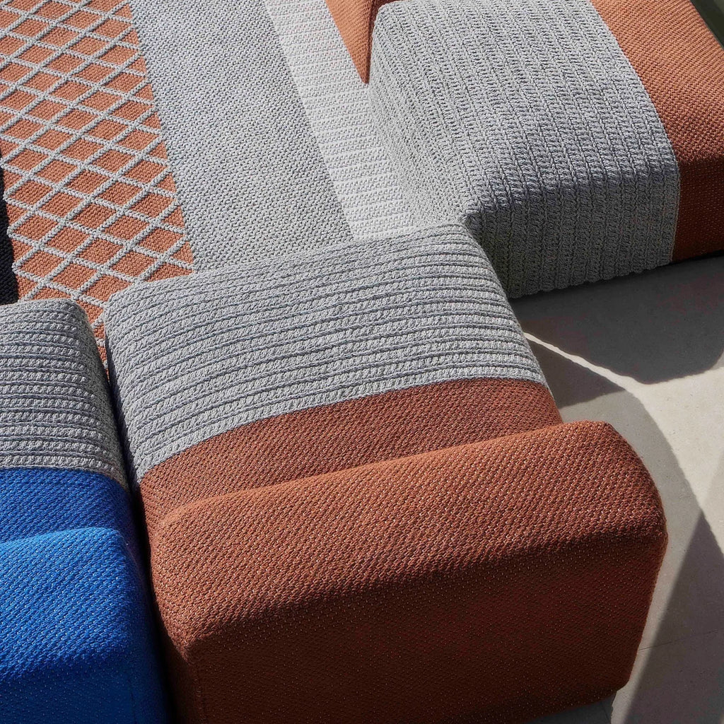 GAN Rugs Mangas Outdoor Composition 2, a contemporary modular outdoor sofa featuring durable hand-knitted fabric upholstery in earthy terracotta, light grey, and vibrant royal blue tones. The multi-textured design showcases ribbed sections, a tight weave, and a distinctive grey diamond pattern against a terracotta background, offering an organic modern aesthetic. Ideal for creating a stylish outdoor living room or versatile patio lounge seating.