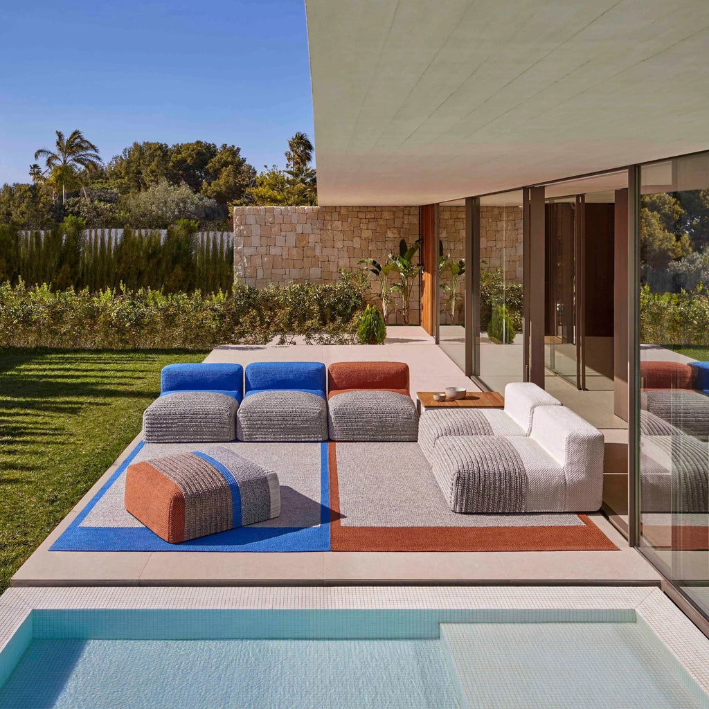GAN Rugs Mangas Outdoor Composition 2, a vibrant modular outdoor sofa featuring hand-knitted textured fabric in a palette of light gray, royal blue, terracotta, and crisp white. This contemporary lounge seating offers a low-profile, organic design with separate backrests and base units, creating flexible configurations for modern outdoor living. Ideal as stylish patio furniture or poolside lounge seating for designer terraces and garden spaces.
