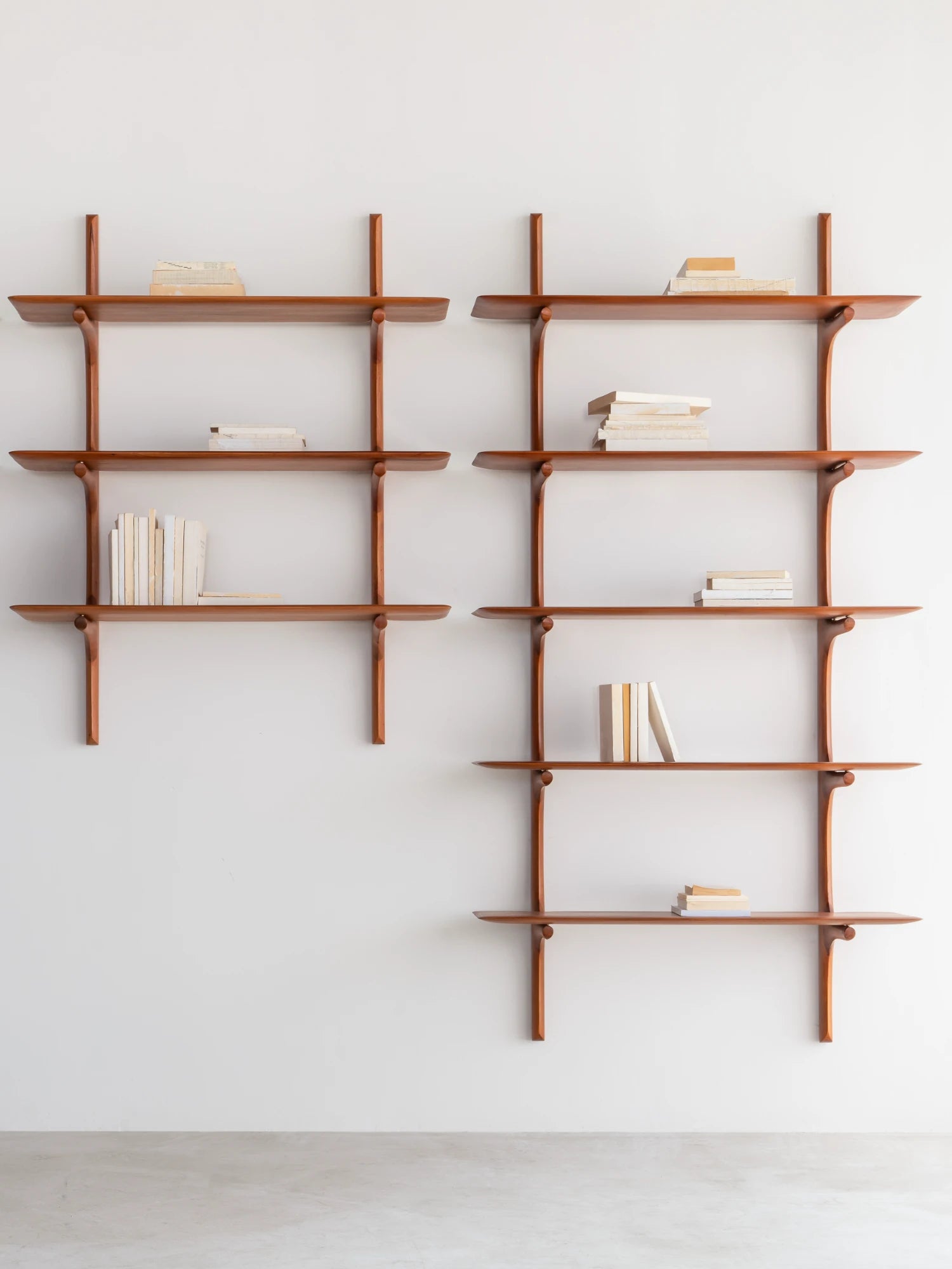 Ethnicraft PI Wall Shelf, a modular mid-century modern solid wood shelving unit featuring warm reddish-brown wood with distinctive curved supports and smooth, elegant floating shelves. This versatile wooden wall shelf system is ideal for minimalist living rooms, Scandinavian home offices, or contemporary bedroom accent styling.