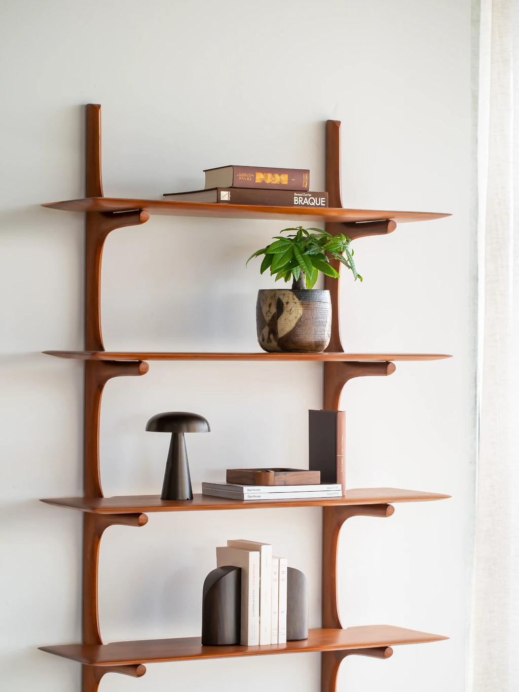 Ethnicraft PI Wall Shelf, a mid-century modern solid wood wall shelf crafted from warm amber-toned wood, featuring an organic design with flowing, sculptural curves.