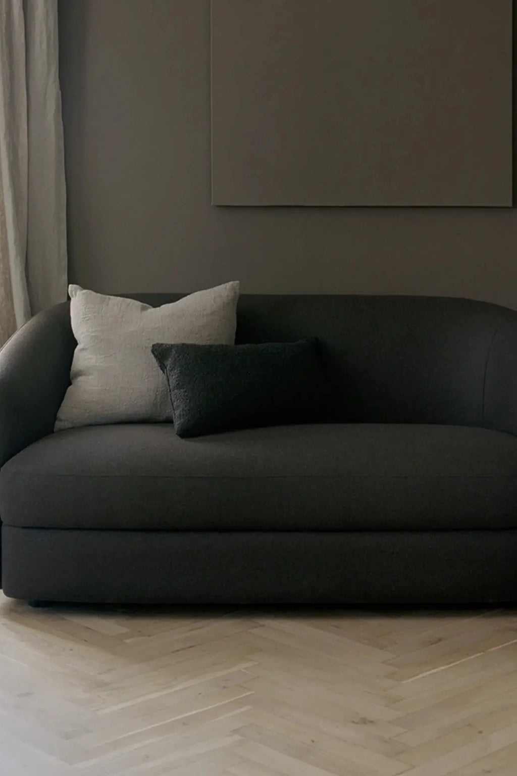 New Works Covent Sofa Narrow 2-Seater, a contemporary dark grey sofa upholstered in a richly textured fabric, featuring a gently curved backrest and rounded armrests that create a soft,.