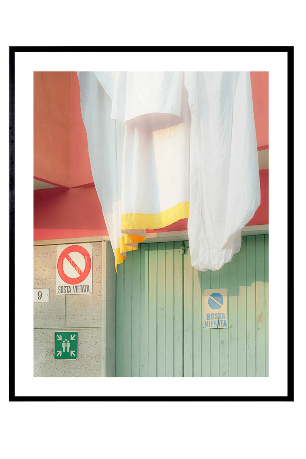 The Poster Club Camogli - Photo Art Print, a vibrant architectural photography print capturing a quintessential Mediterranean street scene with white linen sheets featuring a bright yellow trim, draped over a textured coral-pink wall and.