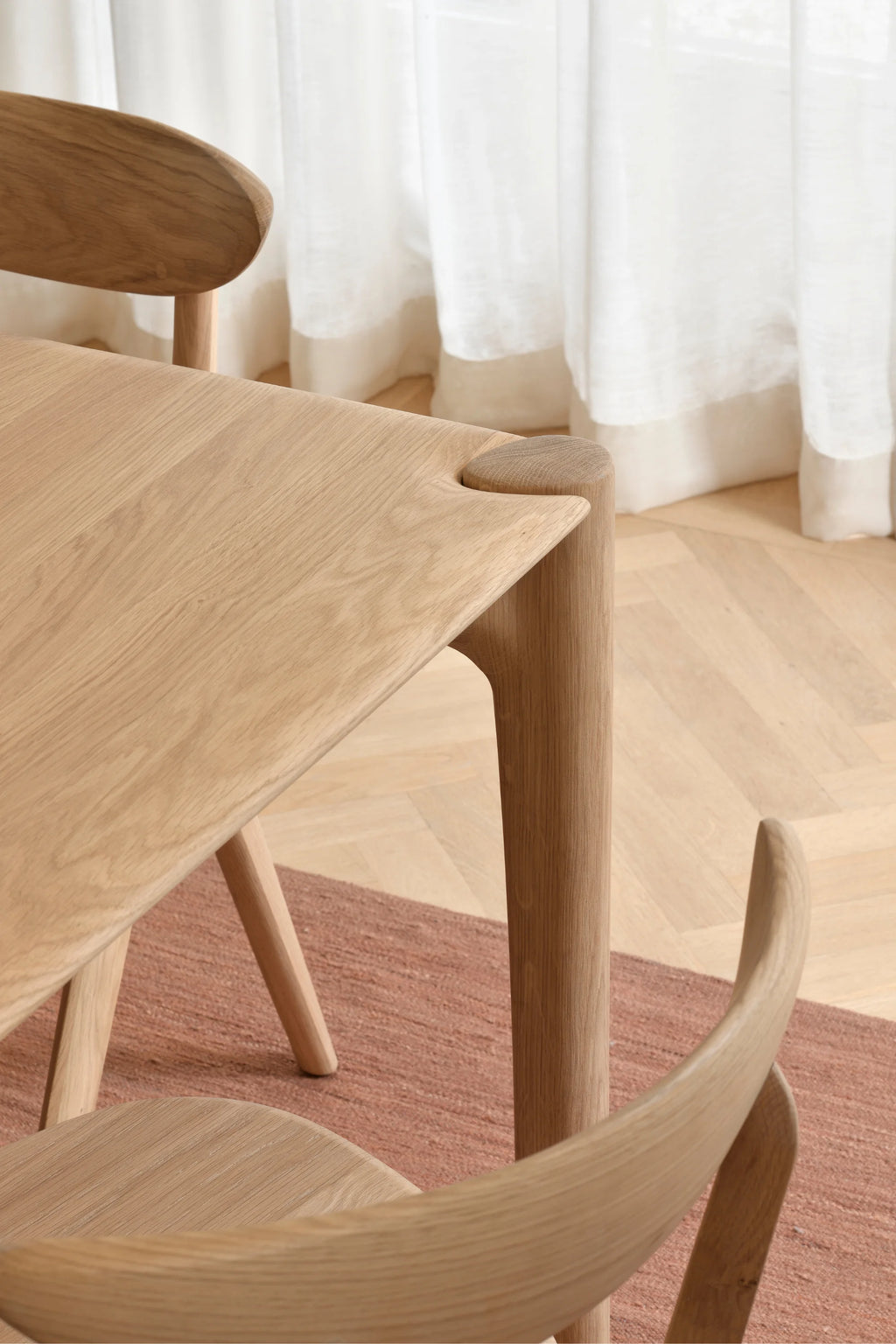 Ethnicraft PI Dining Table, a contemporary solid oak dining table featuring a light natural wood finish with prominent grain and softly rounded corners. Its distinctive organic modern design showcases a unique cylindrical leg integration into the tabletop, creating a seamless and sturdy structure. Ideal for minimalist dining rooms or Scandinavian-inspired kitchen spaces.