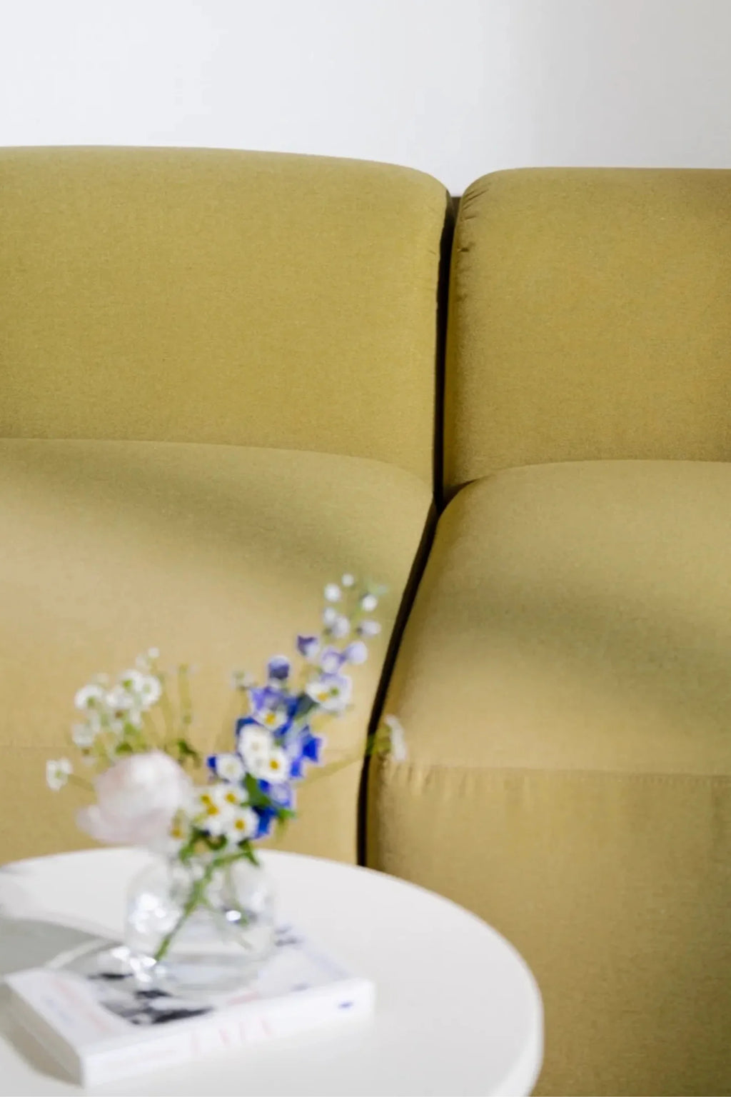 noo.ma Flom Corner Sofa, a plush and inviting contemporary corner sofa upholstered in a muted olive green fabric. It features a modular design with soft, rounded edges and deep, comfortable seating, showcasing a modern organic aesthetic. Ideal for creating a cozy yet stylish focal point in minimalist living rooms or contemporary lounge spaces.
