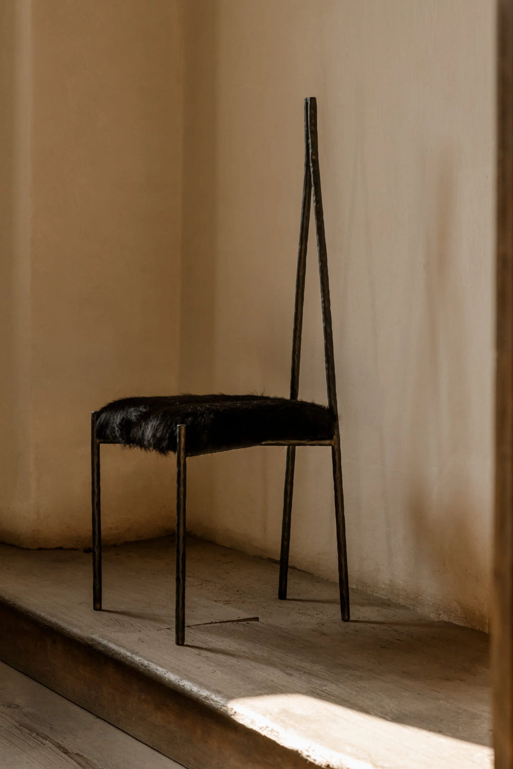 NG DESIGN Object 117 Chair, featuring a luxurious black fur seat on a thin, dark bronze-colored metal frame with an angular, distressed finish and a tall, slender backrest. This authentic, handcrafted statement piece is perfect for a modern living space.