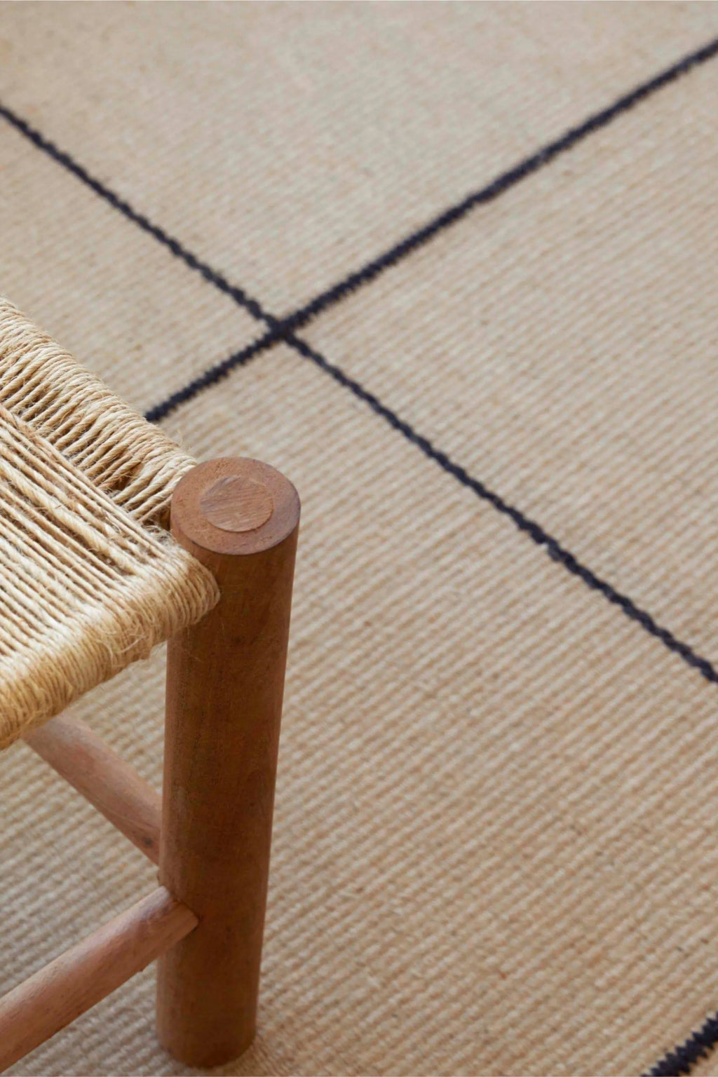 GAN Rugs Roots 001 Rug, a natural beige flatweave rug crafted from robust hand-spun jute fibers, featuring a striking dark navy grid pattern that creates a minimalist yet impactful design. This organic modern rug offers a rustic texture and contemporary aesthetic, perfect for anchoring a Scandinavian living room, japandi bedroom, or bohemian entryway.