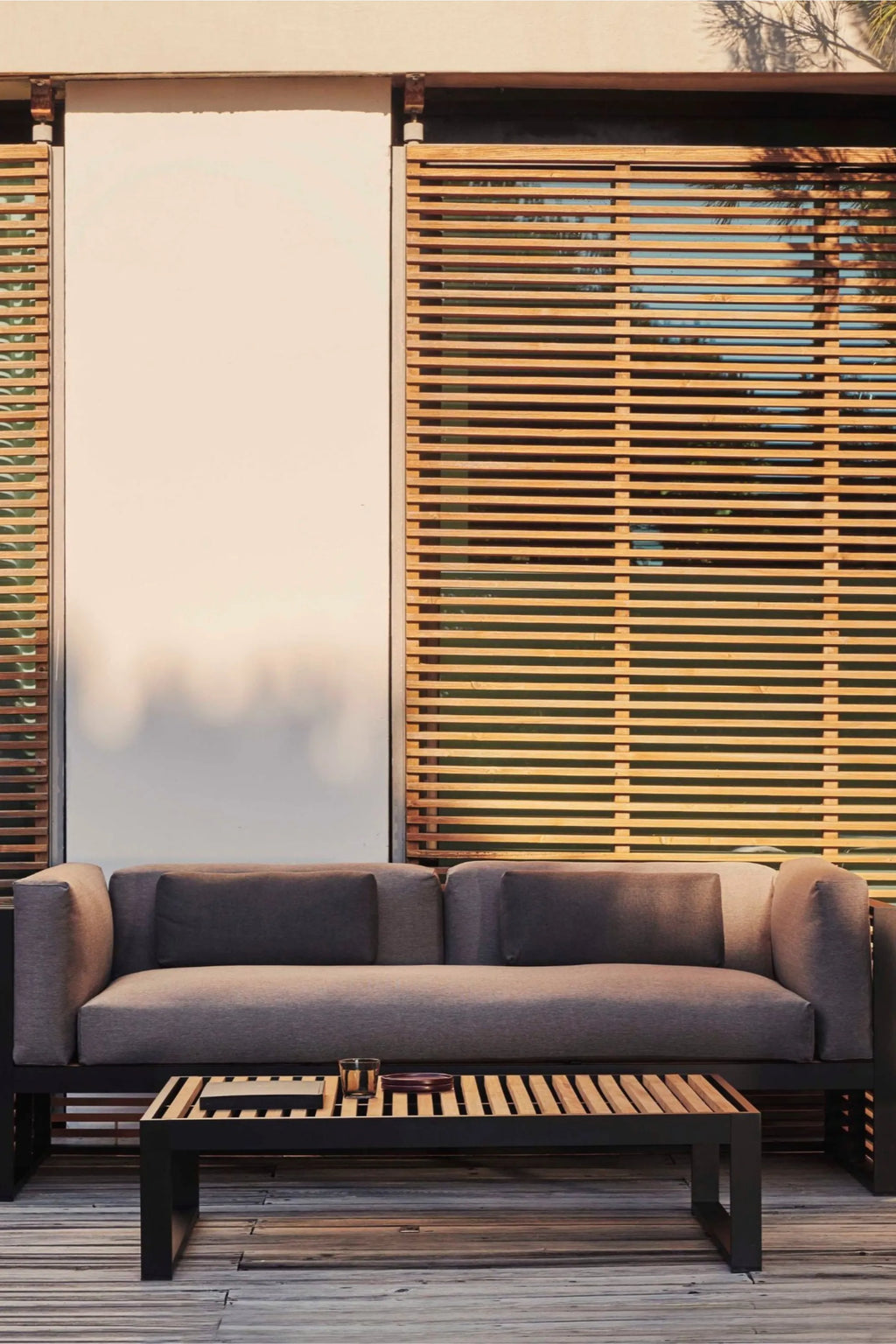 Gandia Blasco DNA Teak 3-Seat Sofa, a modern outdoor sofa featuring a sleek matte black metal frame with warm slatted teak wood accents and plush dark grey fabric cushions. This contemporary 3-seater patio sofa offers minimalist design for luxury outdoor living spaces or a stylish deck.