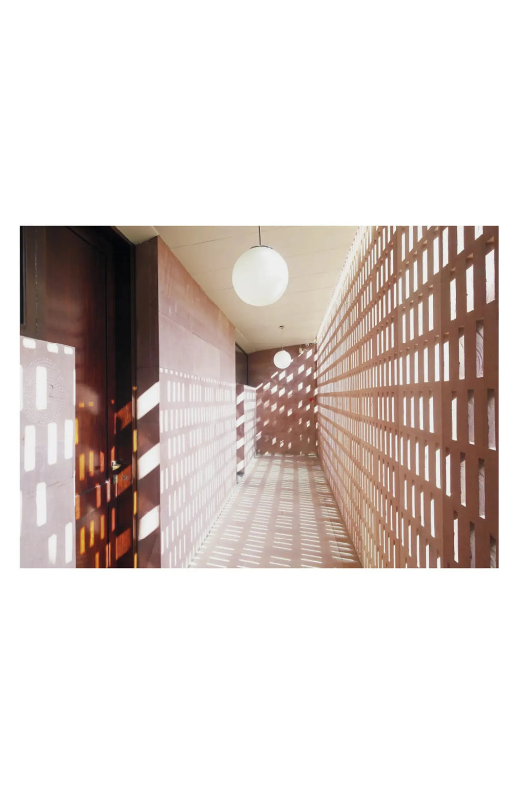 The Poster Club Lights, a captivating architectural poster featuring a long corridor with strong geometric light and shadow patterns cast by a terracotta-toned screen wall. Two white spherical pendant lights illuminate the minimalist space, creating a modernist interior photography print with warm brown and earthy tones.