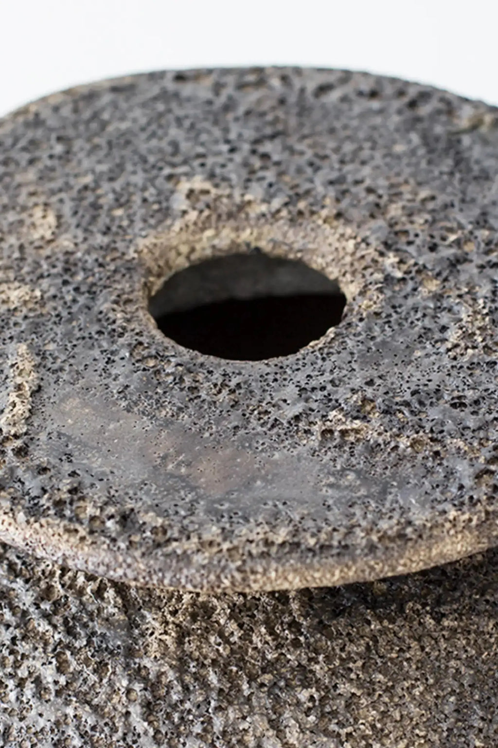 Canoa Lab Isolated n.7 Vase, a dark grey handcrafted stoneware vase featuring an intensely porous, volcanic-like texture and a unique sculptural form with a central circular opening.