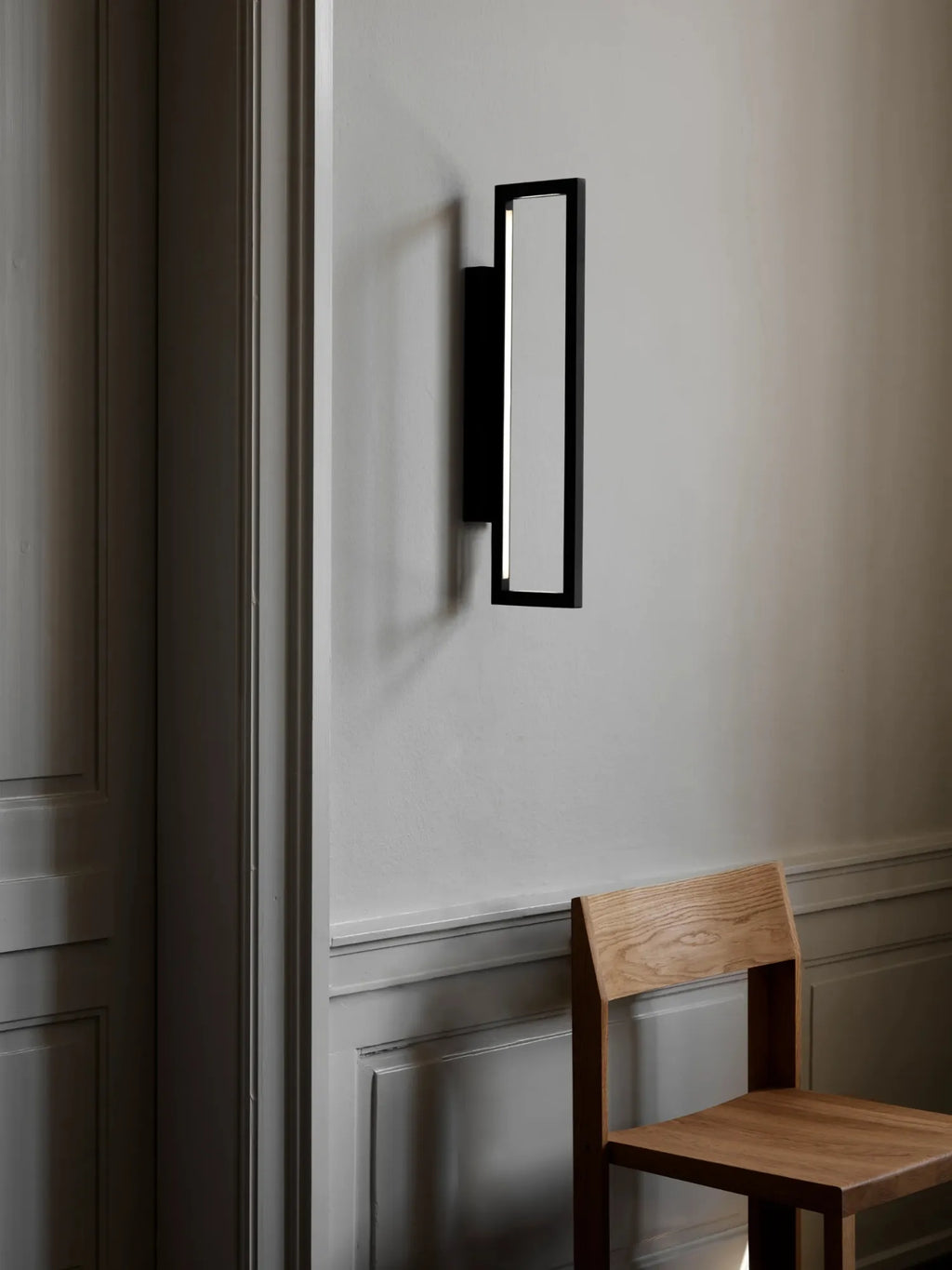 Kristina Dam Geometric Wall Lamp, a sleek modern minimalist wall light featuring a matte black metal frame with a rectangular profile and an integrated LED light strip, casting a soft, contemporary glow. This architectural black wall sconce is perfect for adding understated elegance to Scandinavian living rooms, modern bedrooms, or minimalist hallways and entryways.