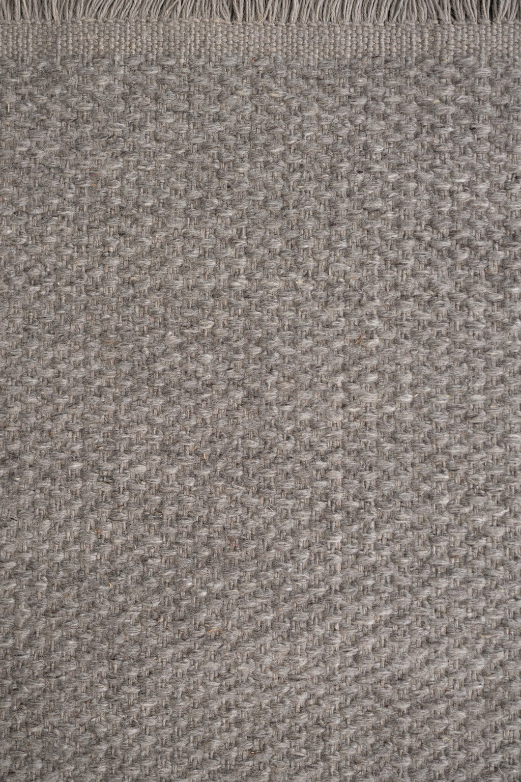 Linie Design Pastoral Unity Wool Rug, a premium hand-woven wool area rug crafted with a dense, textured bouclé-like weave in natural heather grey and oatmeal tones with subtle organic variations. This durable and sustainable rug features a classic fringed edge, embodying a blend of organic modern and Scandinavian design. Ideal for adding warmth and sophisticated texture to minimalist living rooms, cozy bedrooms, or inviting entryways.