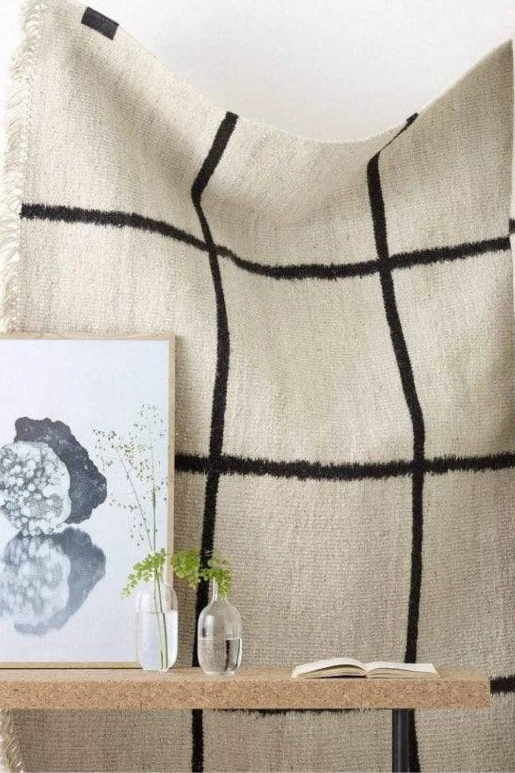 Sera Helsinki Kuura Rug, a modern minimalist hand-knotted wool area rug featuring a cream-colored textured weave with a bold, shaggy deep black grid pattern and delicate fringed edges. This Scandinavian-inspired rug is perfect for adding warmth and an organic modern touch to living rooms, bedrooms, or cozy reading nooks.