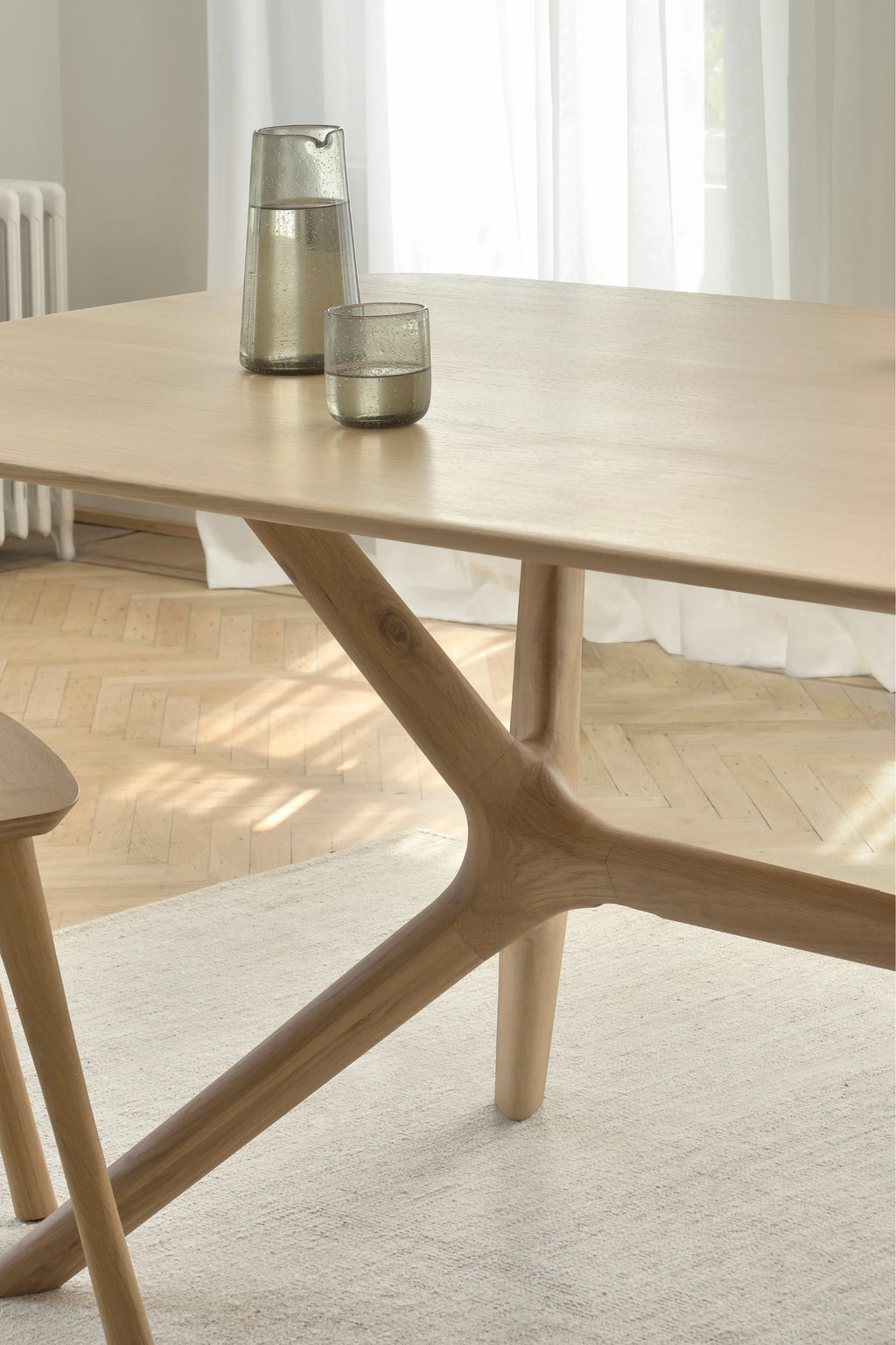 Ethnicraft X Dining Table, a light natural solid oak dining table featuring a smooth, subtly grained rectangular top with rounded edges and a distinctive organic-shaped X-leg base. Its contemporary Scandinavian design and natural wood finish make it ideal for modern dining rooms, open-plan living spaces, or minimalist kitchens.