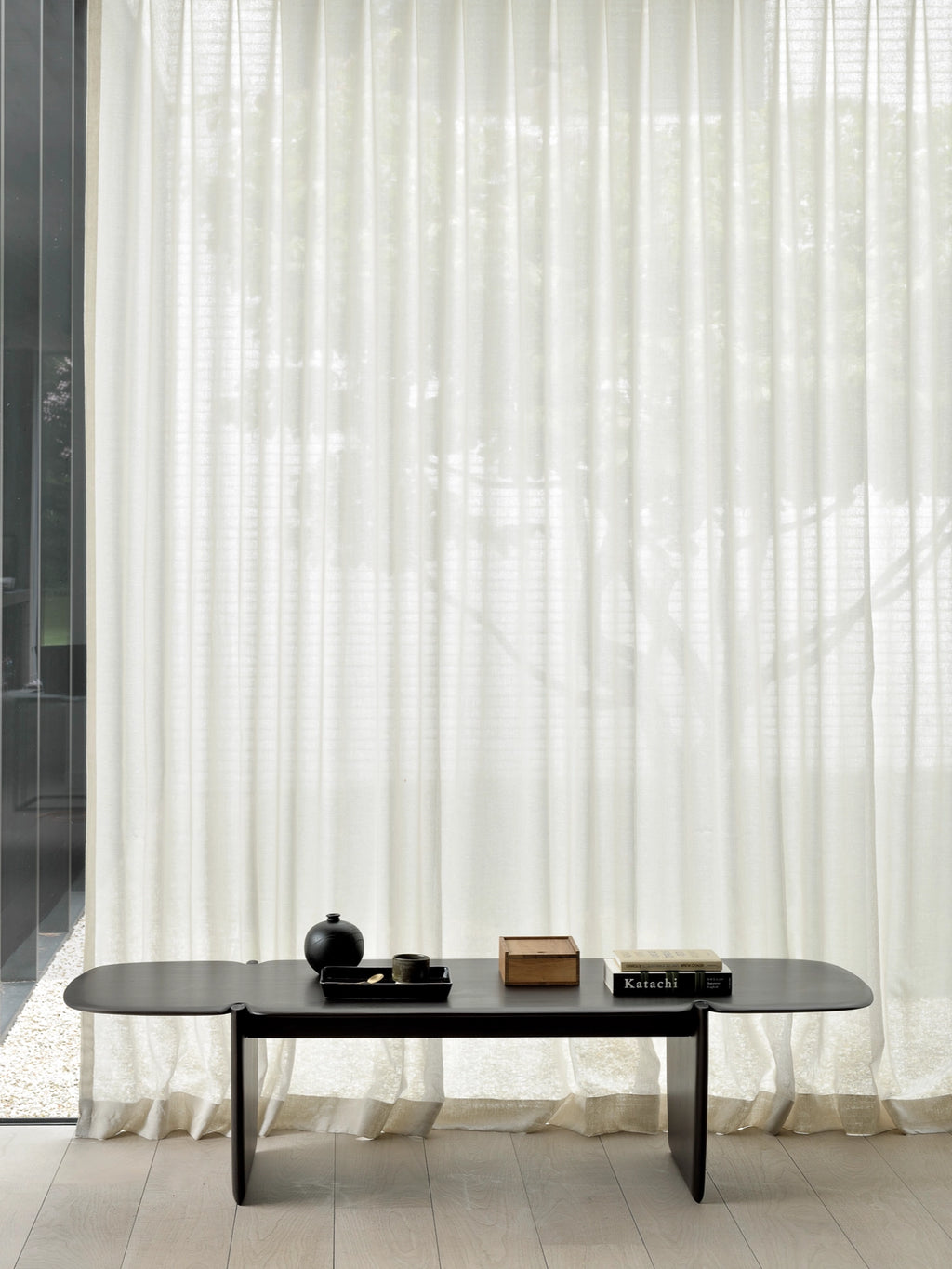 Ethnicraft PI Coffee Table, a sleek, dark brown rectangular wooden coffee table with a minimalist design and sturdy, flat legs, styled with decorative items in a contemporary room with sheer white curtains.
