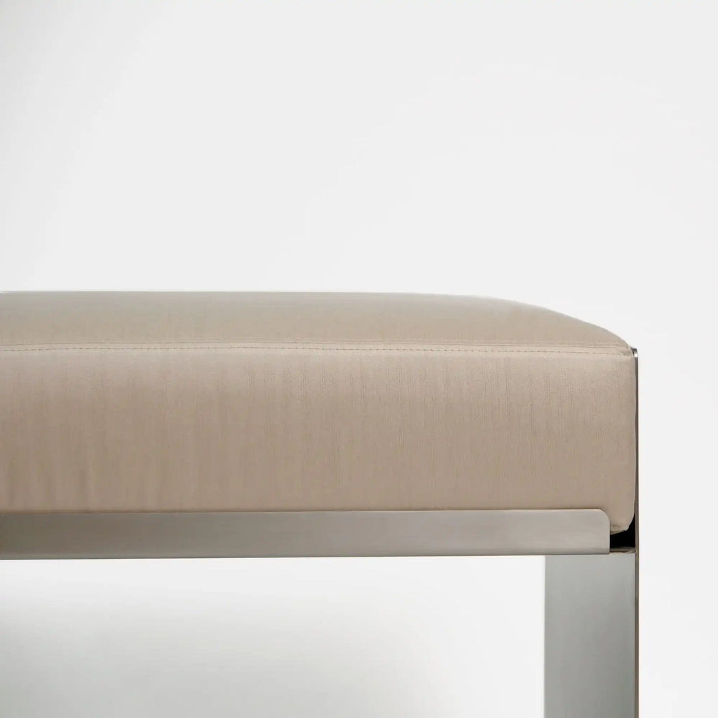 Around Works C.01 Lounge, a modern minimalist pouf featuring a soft, rectangular upholstered top in a light greige fabric with a subtle vertical weave texture and elegant topstitch detail. This contemporary ottoman is supported by a sleek, brushed stainless steel base, creating a clean, architectural profile perfect for modern living rooms, minimalist bedrooms, or stylish entryways.