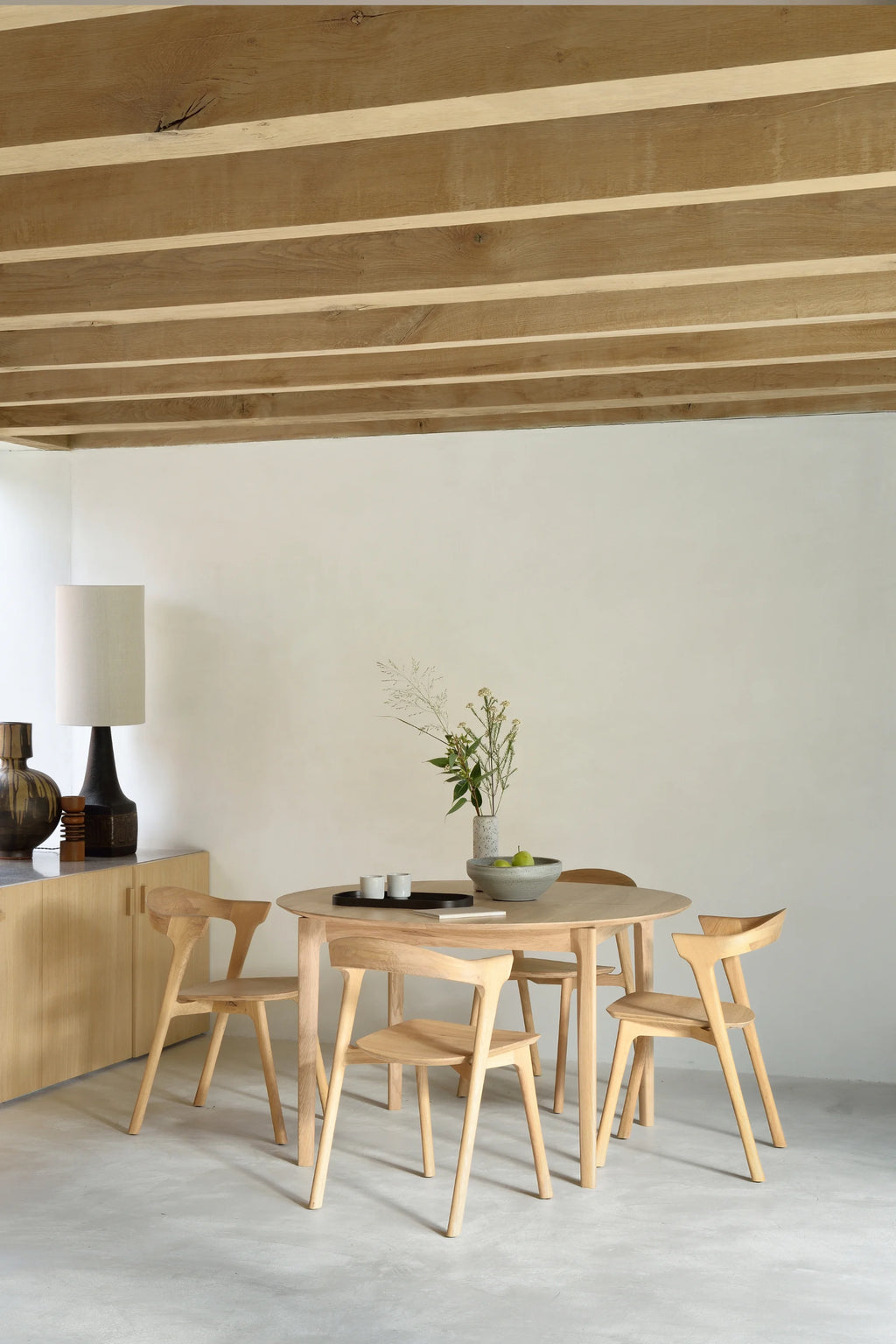Ethnicraft Bok Extendable Dining Table, a minimalist round dining table crafted from light natural solid oak with a smooth finish and elegant tapered legs. Its clean Scandinavian design highlights the beautiful wood grain, offering a versatile aesthetic. Perfect for contemporary dining rooms or Japandi-inspired spaces, this solid oak table combines functionality with organic modern style.
