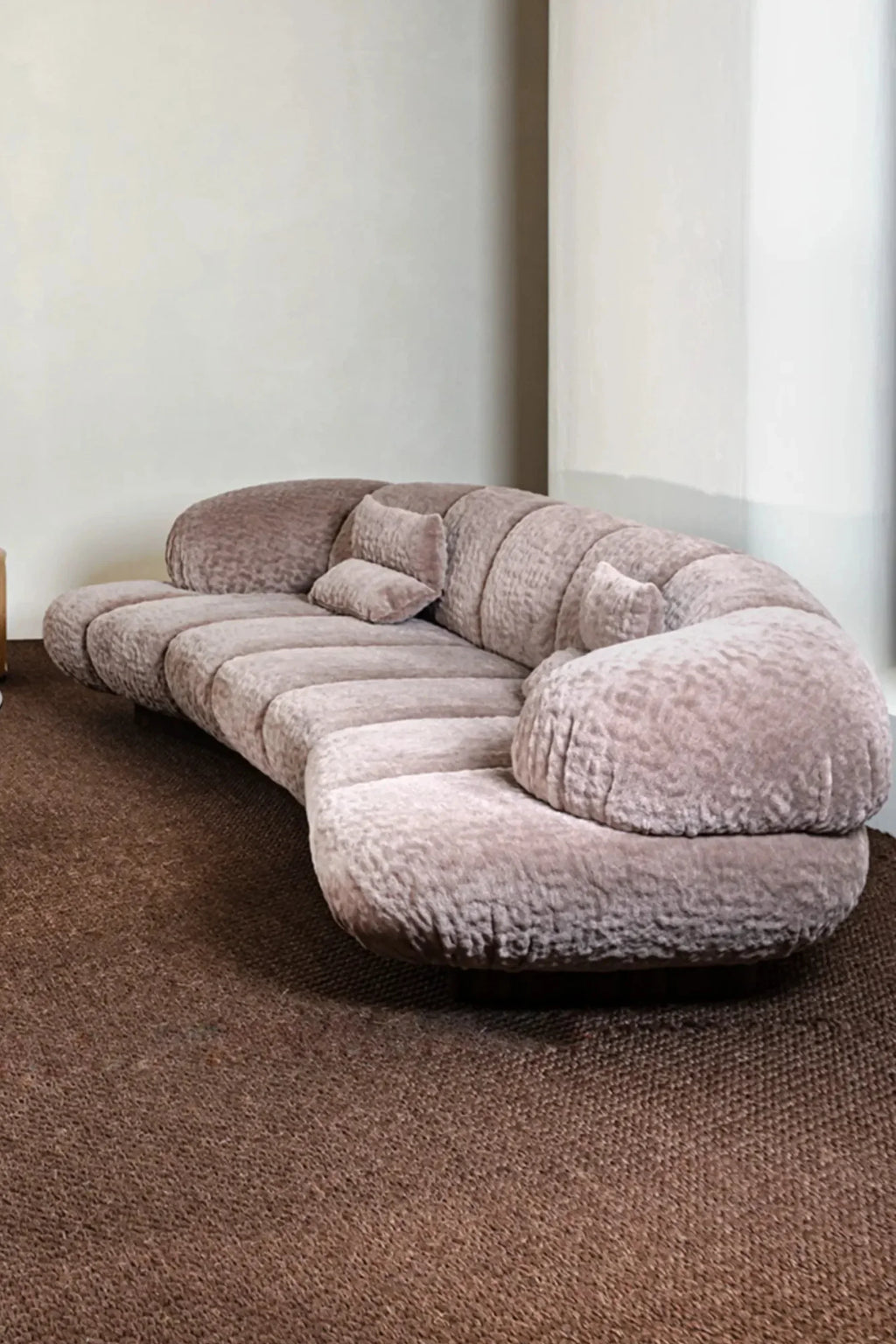 Hessentia Kiro Long Sofa, a luxurious, low-profile curved sofa upholstered in a plush dusty rose bouclé fabric with a highly textured finish and distinctive horizontal channeling.