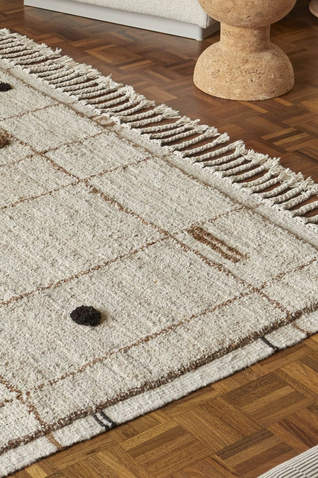 Sera Helsinki Virta Rug, a hand-knotted wool area rug featuring a plush, textured cream-colored pile with natural variations. It showcases an organic, grid-like pattern of thin brown lines and scattered dark brown dots, bordered by soft fringed edges. This minimalist and organic modern rug is perfect for adding warmth to Scandinavian living rooms, cozy bedrooms, or japandi-inspired spaces.
