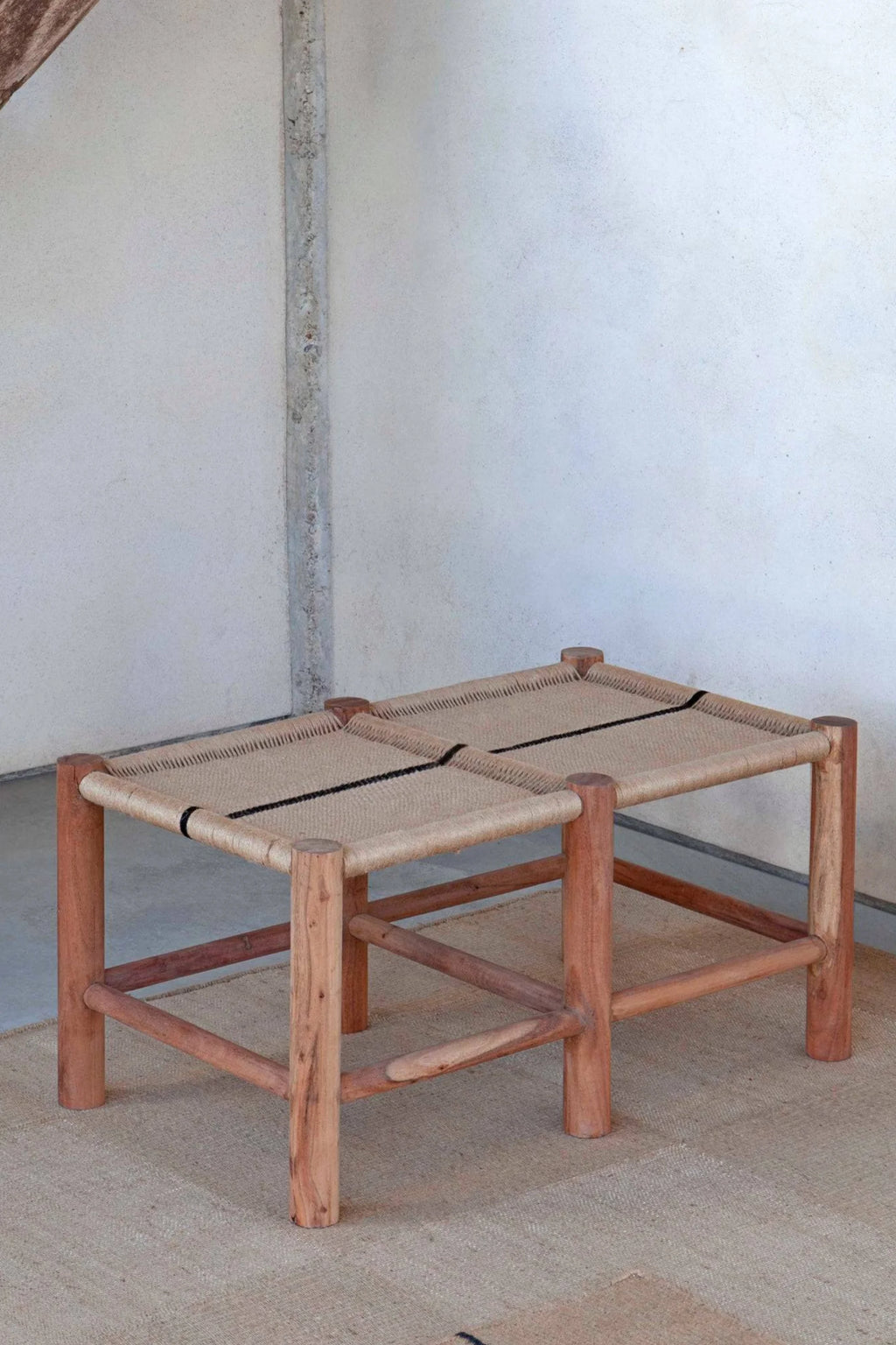 GAN Rugs Roots 01 Bench, a rustic organic modern bench featuring a robust solid wood frame in warm reddish-brown tones with sturdy cylindrical legs and stretchers. It has a handcrafted natural woven fiber seat in a light beige, accented by a distinct black stripe woven through the center. This minimalist wooden bench is perfect for entryway seating, a living room accent, or as a functional bedroom bench in organic modern or wabi-sabi interiors.