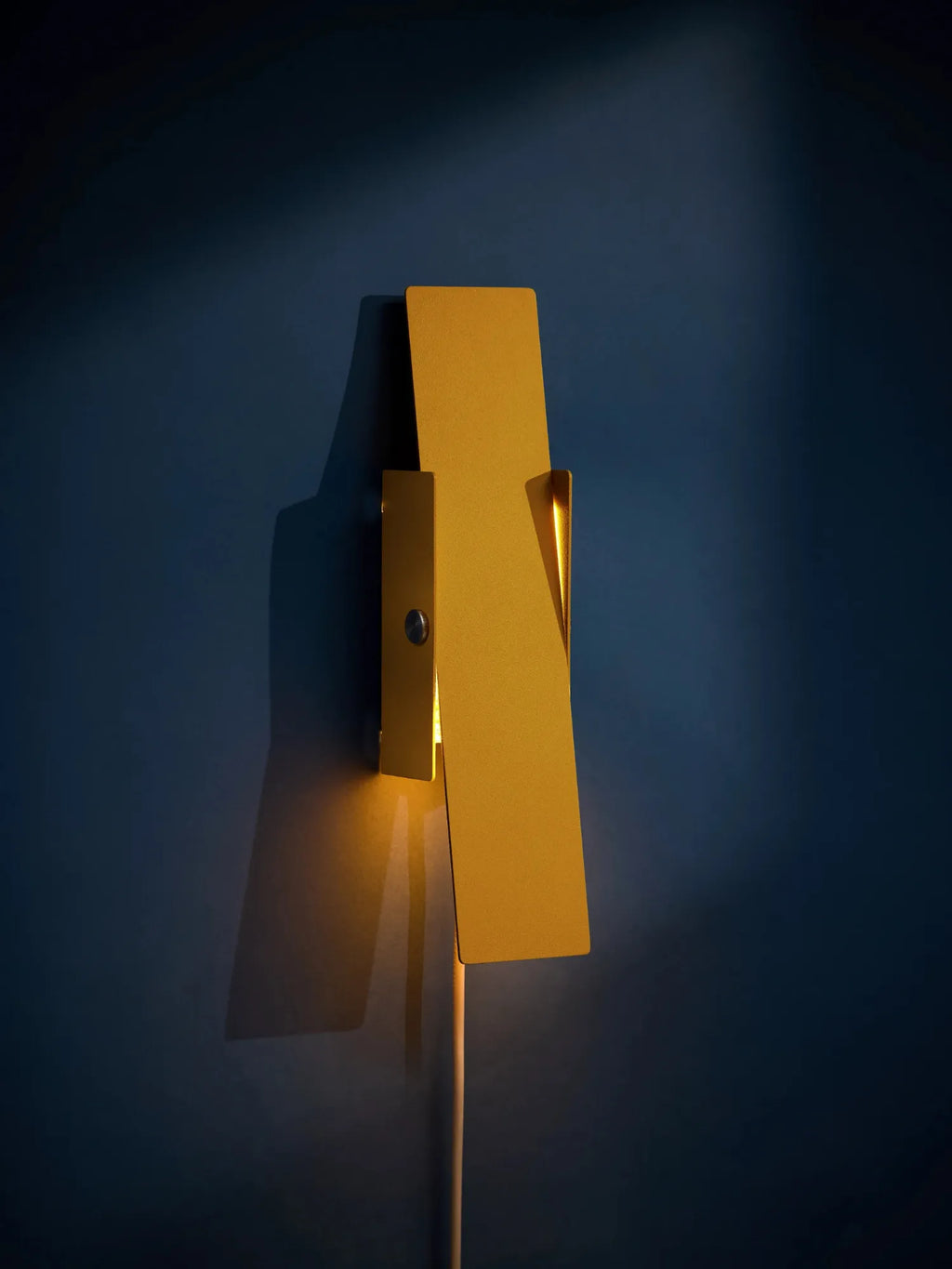 MOEBE Pivoting Wall Lamp, a modern minimalist wall light crafted from matte golden yellow metal with a sleek, geometric design. This unique wall sconce features a rectangular panel that elegantly pivots, directing soft, indirect light to create a warm ambiance. Perfect as Scandinavian accent lighting for contemporary living rooms, bedrooms, or sophisticated home office spaces.