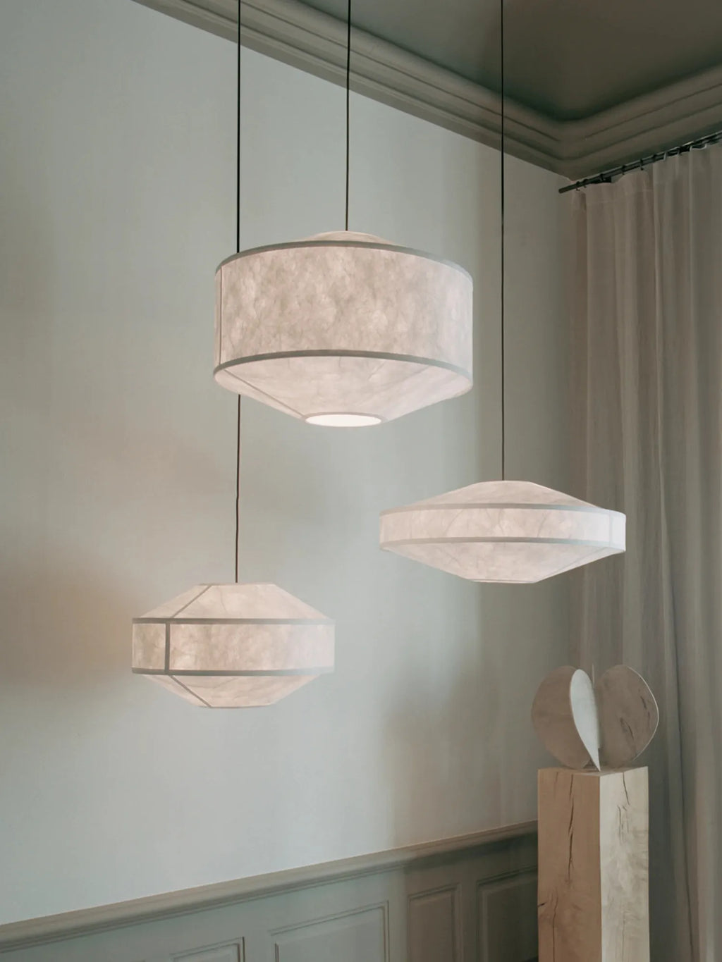 New Works Kite Pendant Lamp featuring three modern, geometric fabric drum shades in a translucent, textured off-white material with slim grey framing, suspended at varying heights in a minimalist setting. Perfect for elegant ambient lighting.