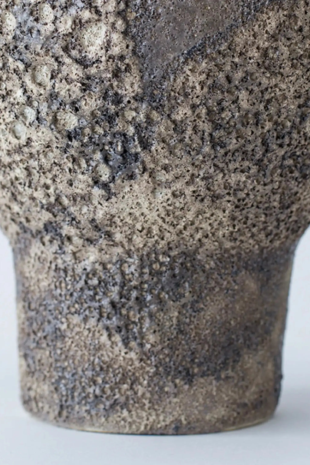 Canoa Lab Isolated n.7 Vase, a handcrafted stoneware vase featuring a deeply textured, porous volcanic finish in mottled dark grey and beige tones, with an organic, rustic silhouette. This artisanal piece is ideal for wabi-sabi or brutalist shelf styling and contemporary organic modern interiors.