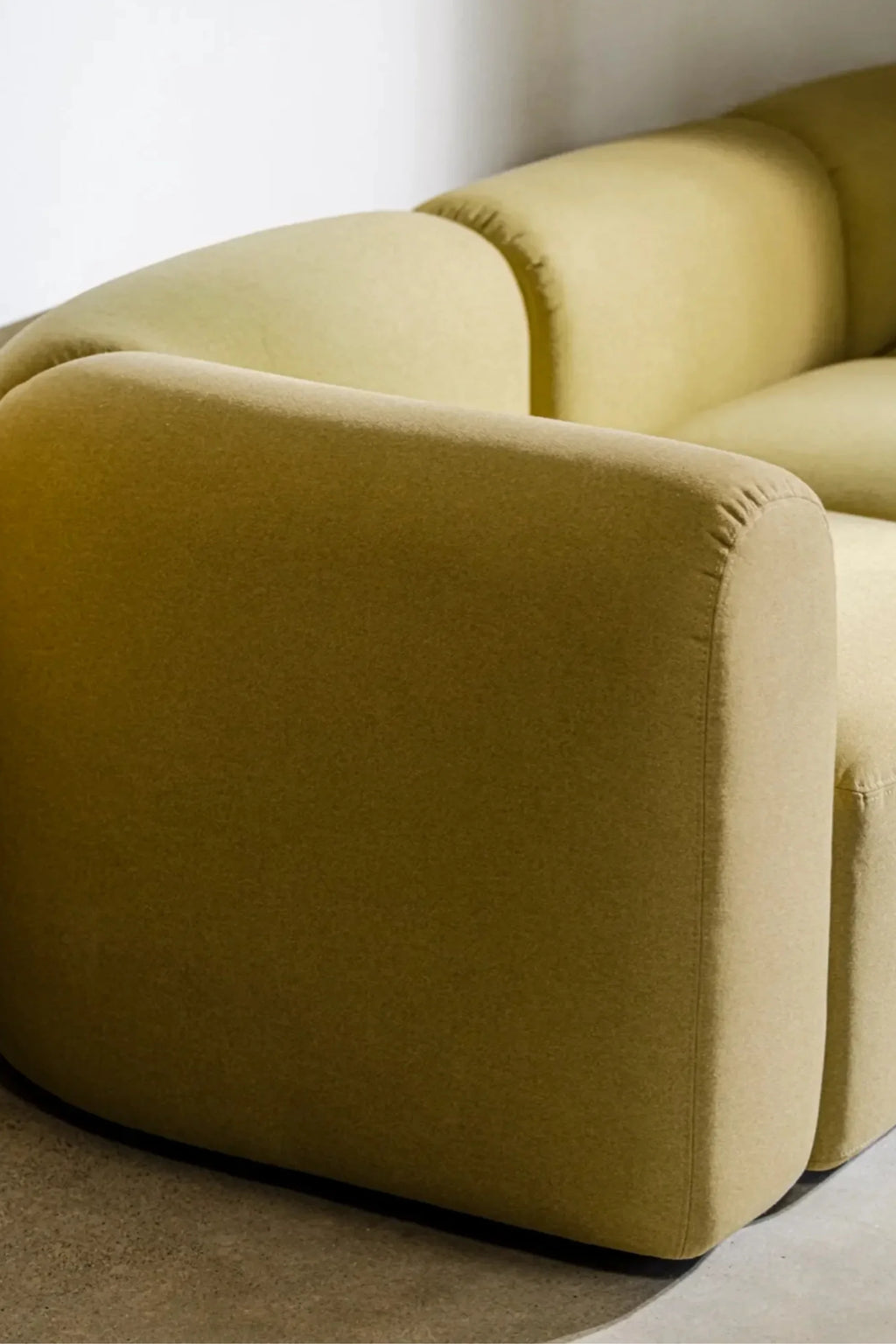 noo.ma Flom Corner Sofa, a contemporary modular corner sofa upholstered in a rich olive green fabric with a soft, inviting texture and distinct rounded, organic forms. Its plush, deep seating and clean lines create a modern minimalist aesthetic. Ideal for a stylish living room or an organic modern interior seeking a statement piece.