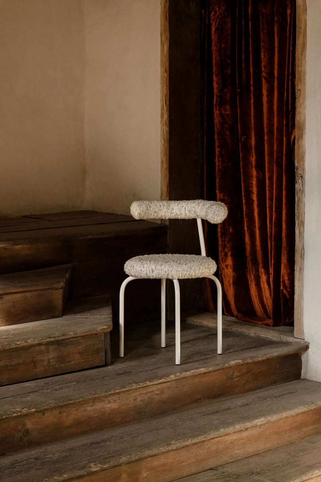 NG DESIGN Object 114 Chair, a premium modern chair with rounded off-white metal legs and ivory bouclé fabric seat and backrest, displayed on aged wooden stairs with a rich red velvet curtain in the background. Ideal as a contemporary accent piece.
