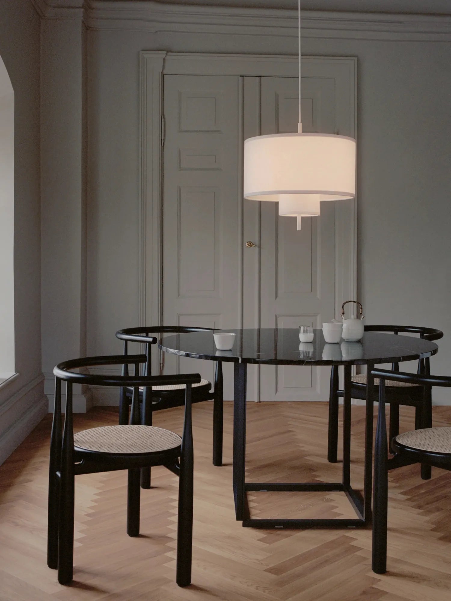 New Works Margin Pendant Lamp with a multi-tiered white textile shade, softly illuminating a modern dining area with a black marble-top table and matching chairs. A luxury lighting fixture for elegant interior design.