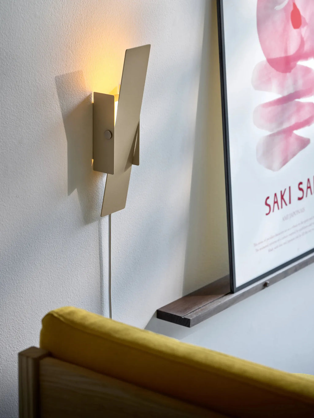 MOEBE Pivoting Wall Lamp, a modern minimalist wall light crafted from matte beige powder-coated metal, featuring a unique folded geometric design that allows the light source to pivot and direct illumination. This contemporary wall sconce has a visible plug-in cord, offering flexible installation for Scandinavian bedrooms, living rooms, or home office spaces.