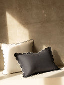 Two decorative pillows with scalloped edges, one white and one gray, on a textured surface.