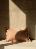 Scalloped-edge pillow on a textured surface with a light beam casting a shadow.