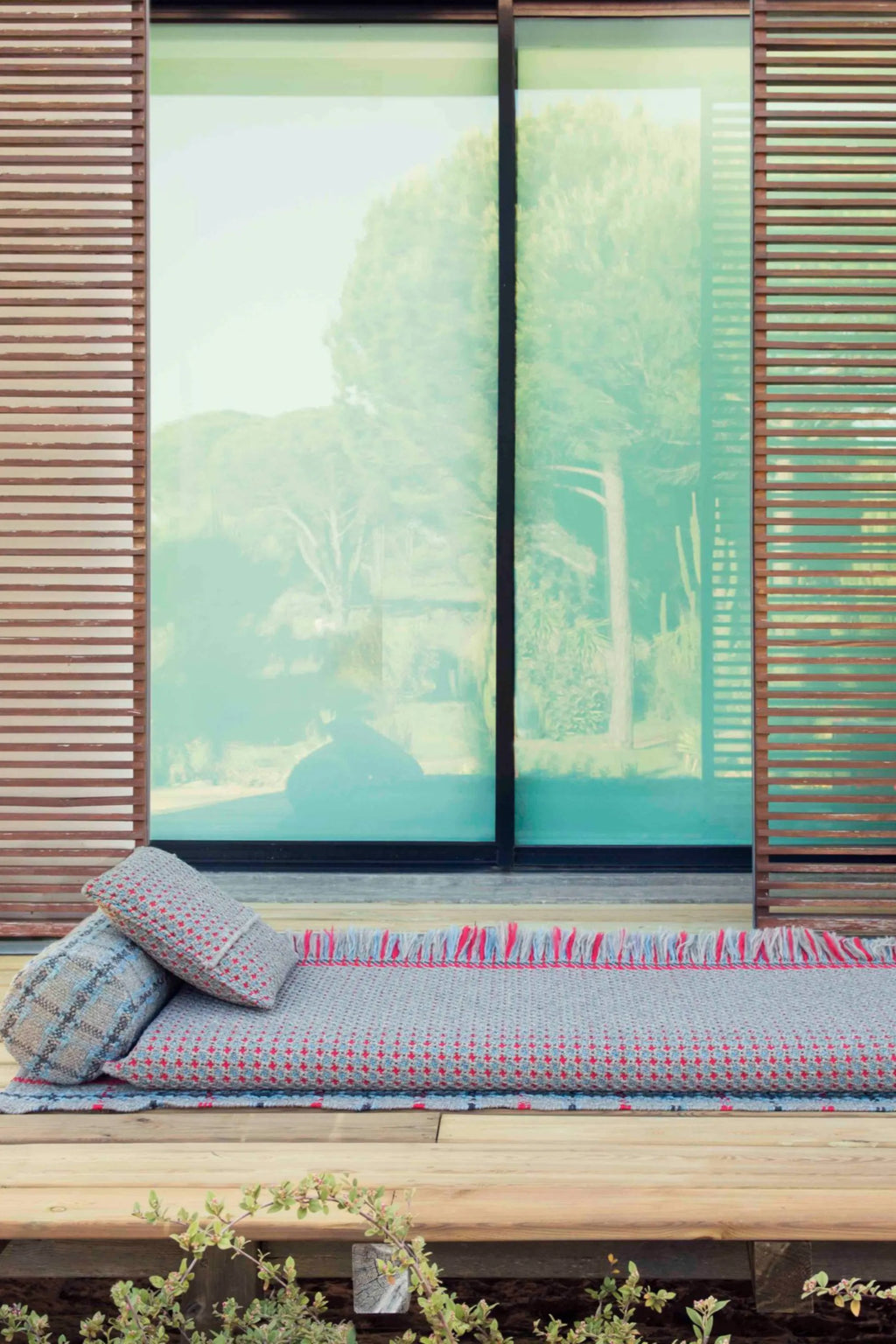 GAN Rugs Garden Layers Composition 05, a contemporary low-profile outdoor sofa and lounge set featuring a durable woven fabric base in light grey with a vibrant red and blue geometric pattern and playful fringed edges.