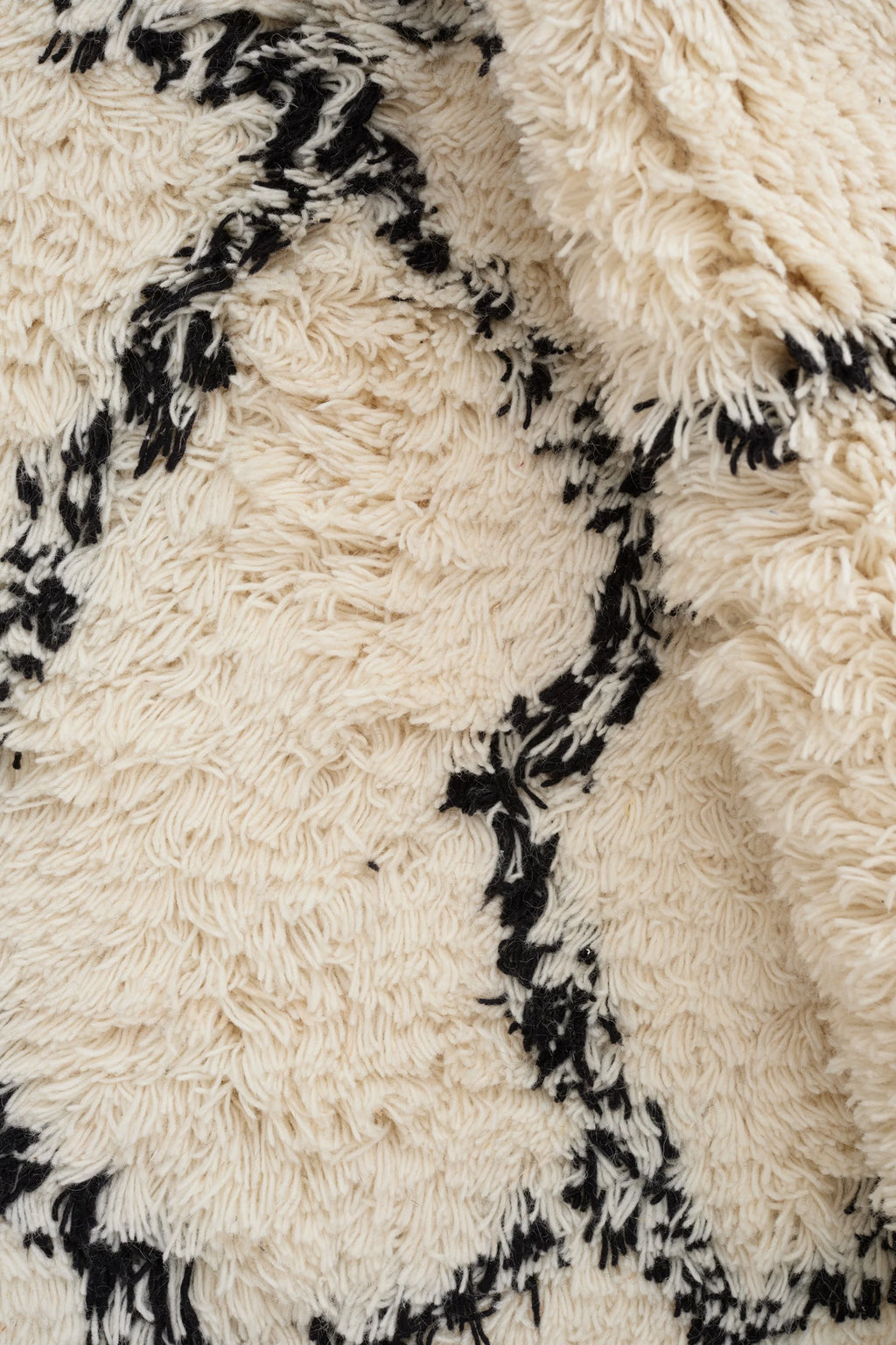 Linie Design Ruffle Wool Rug, a plush hand-knotted wool area rug featuring a high-pile shaggy texture in natural cream with bold abstract black patterns. Its soft, thick weave and monochrome design make it a versatile statement piece, perfect for adding warmth and bohemian elegance to Scandinavian living rooms, minimalist bedrooms, or contemporary spaces.