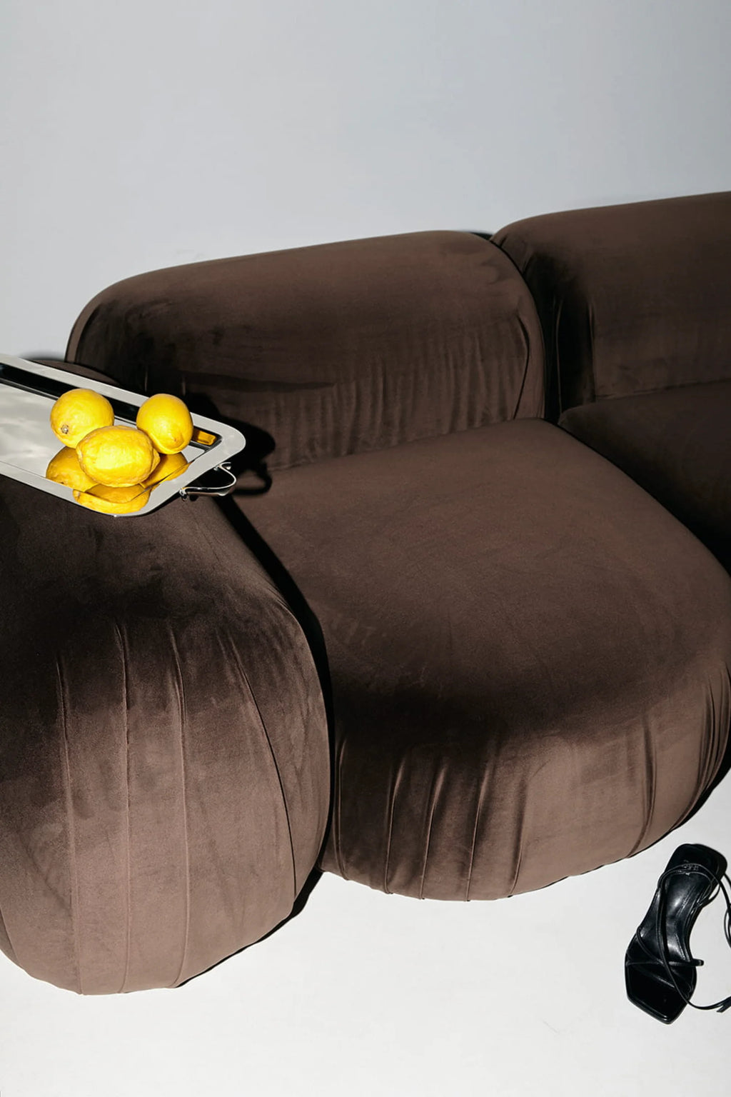 NG DESIGN Object 103 Armchair in a luxurious dark brown velvet, showcasing its plush, modular design. A silver tray with lemons rests on the arm, adding a fresh contrast. Ideal for modern living spaces.