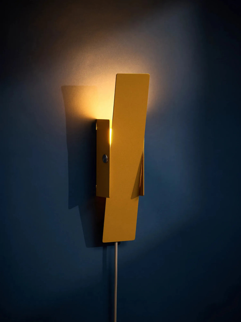 MOEBE Pivoting Wall Lamp, a modern minimalist wall light crafted from matte mustard yellow metal with a striking geometric, angled design and a functional pivoting mechanism. This contemporary wall sconce provides adjustable accent lighting, perfect for a Scandinavian living room, bedroom, or home office.