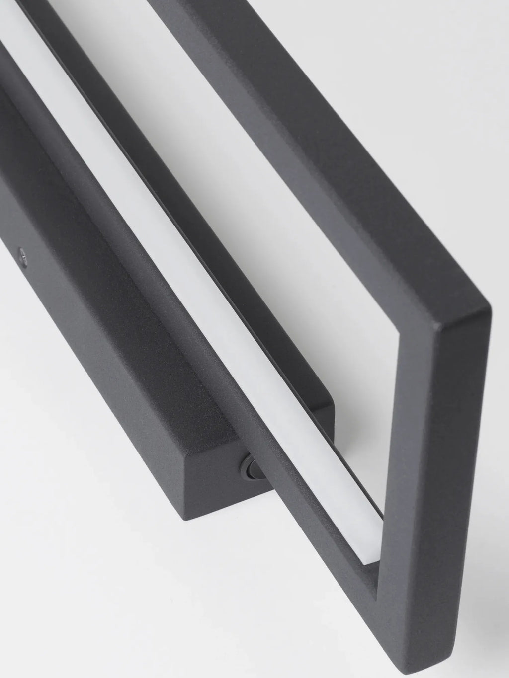 Kristina Dam Geometric Wall Lamp, a matte black metal wall light with a textured finish, featuring a bold open rectangular frame and a linear integrated LED light strip. This modern minimalist wall sconce offers industrial chic appeal, perfect for contemporary entryways, living rooms, or brutalist-inspired spaces.