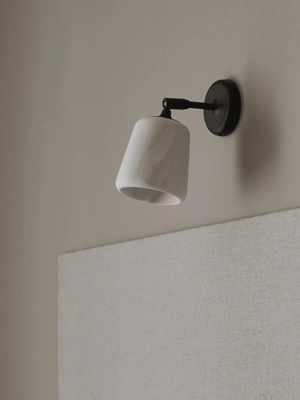 New Works Material Wall Lamp: Elegant sconce with a raw white marble cone shade featuring subtle grey veining and a matte black metal base, mounted on a neutral wall. A luxurious lighting fixture for refined interior spaces.