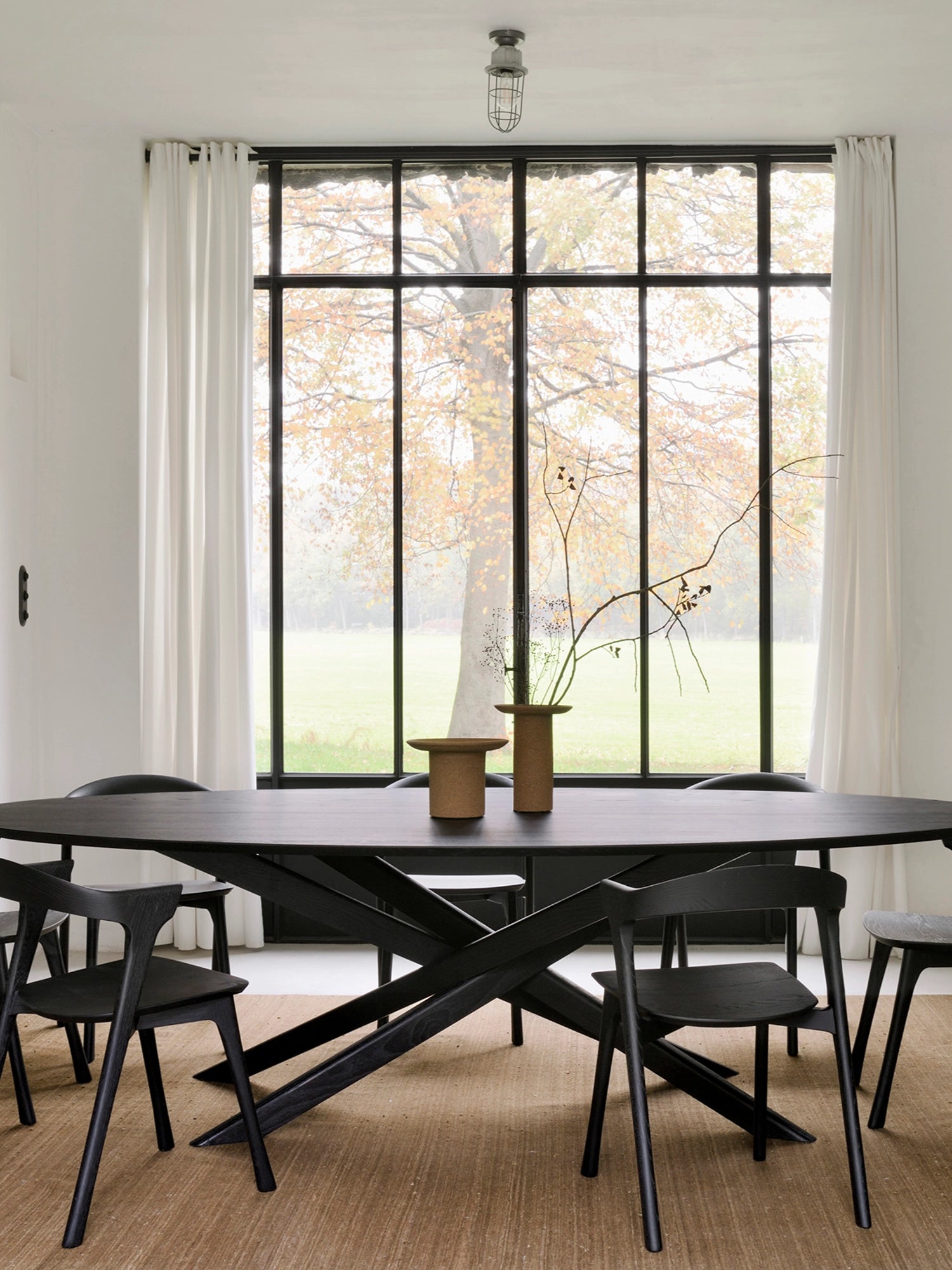 Ethnicraft Mikado Dining Table, a large contemporary oval dining table crafted from solid black-stained oak, featuring a distinctive crisscross X-shaped base that creates a sculptural and modern minimalist aesthetic. This elegant black wood dining table is perfect for a spacious modern dining room or an organic modern interior seeking a statement piece.