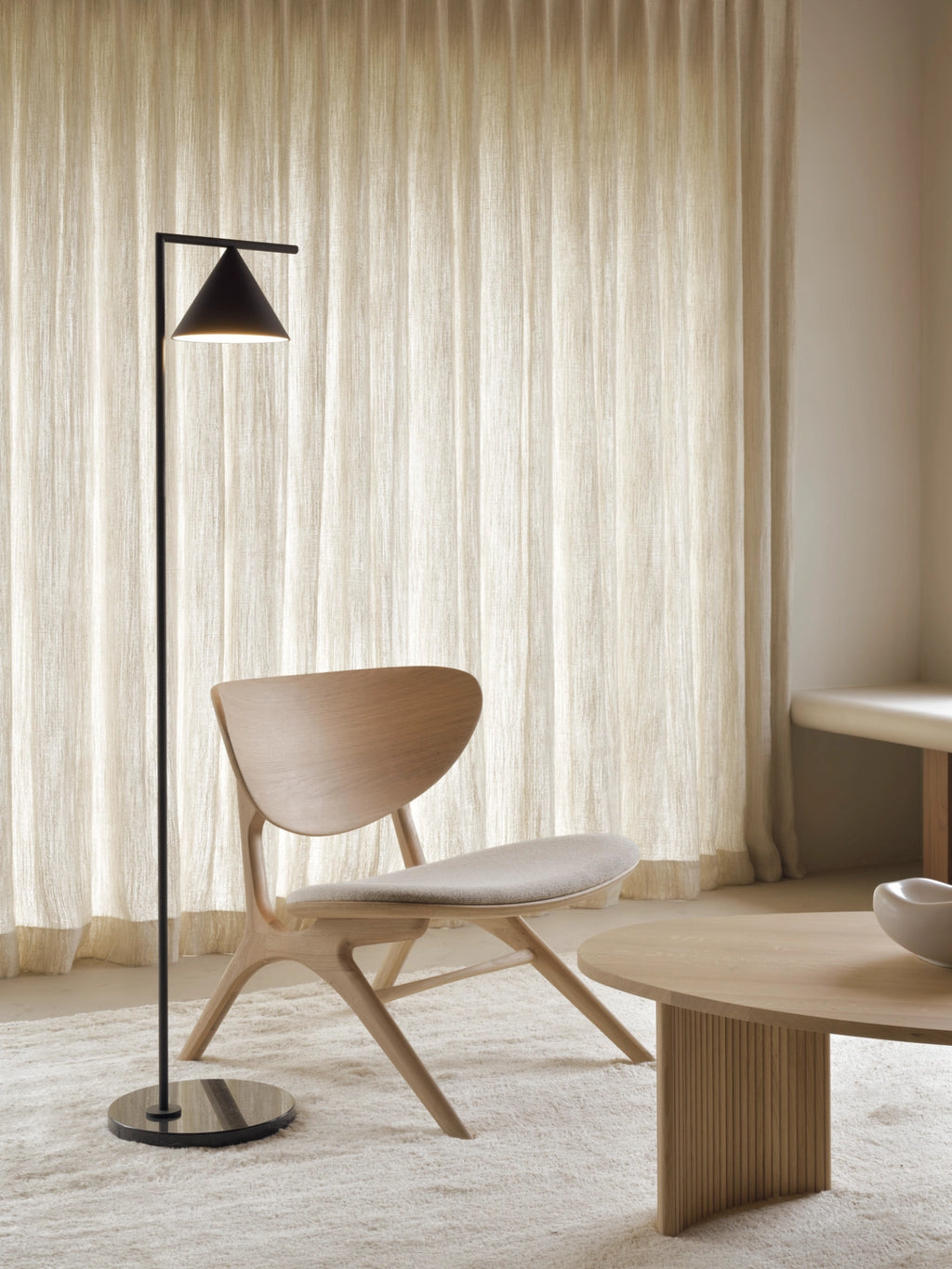 Ethnicraft Eye Lounge Chair, a Scandinavian-inspired solid light oak lounge chair featuring a gracefully curved, sculptural backrest, distinct angled legs, and a comfortable light grey fabric upholstered seat.