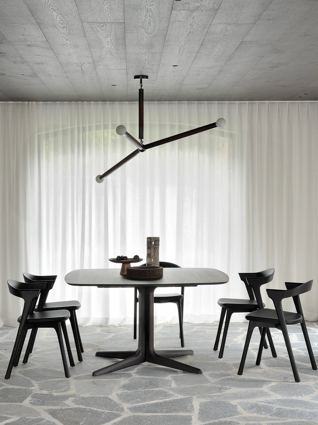 Ethnicraft Corto Dining Table in square oak brown, showcasing its elegant natural wood grain and sturdy pedestal base, presented in a modern dining room setting with chairs.